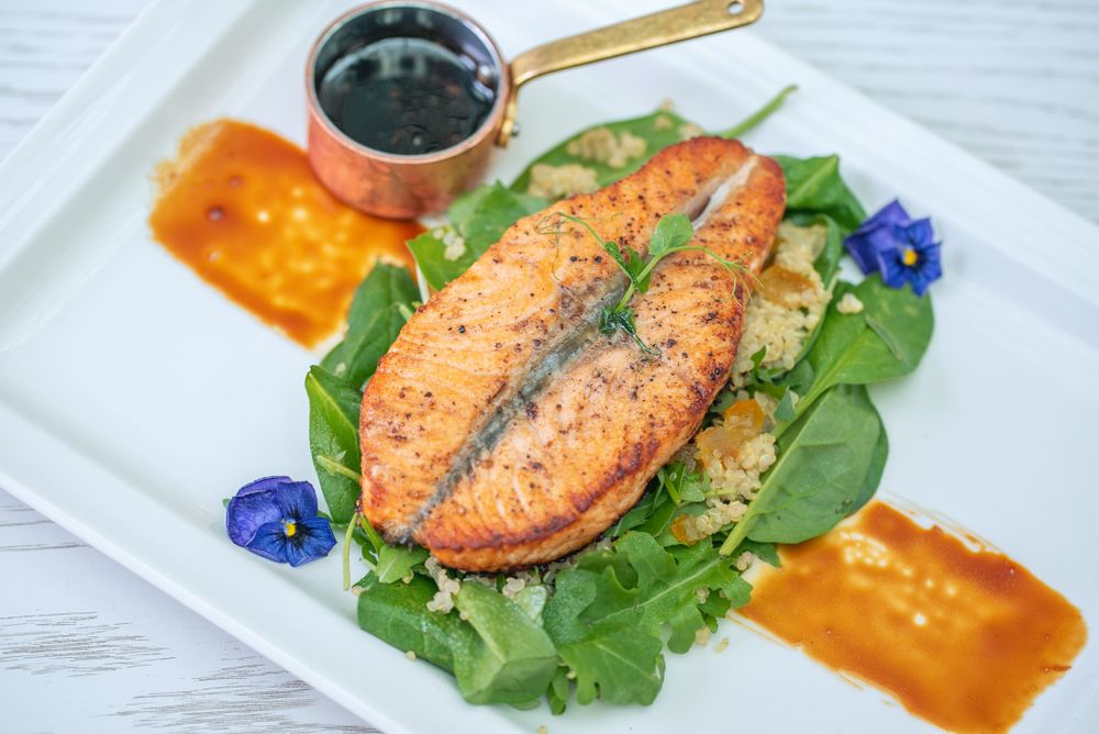 Pavé de saumon poêlé sur quinoa et roquette, fleurs comestibles, dressé en gastronomie